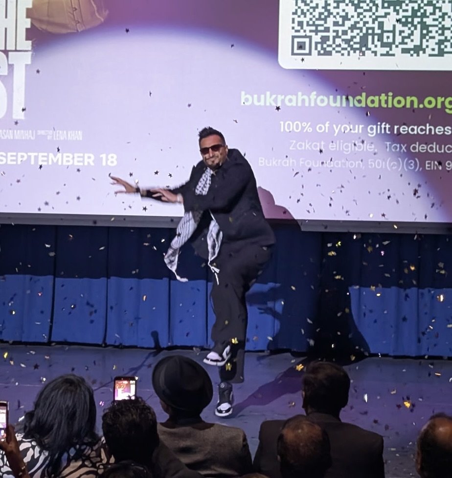 Asim Khan on stage under falling confetti while emceeing a screening fundraiser