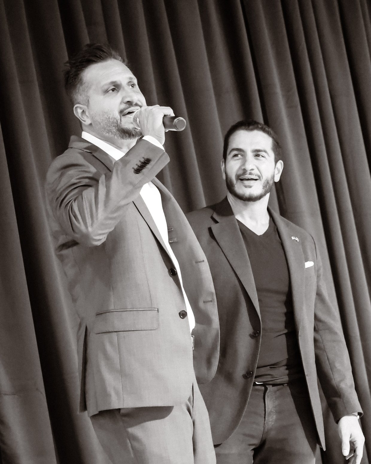 Asim Khan on stage with a microphone beside Abdul El-Sayed