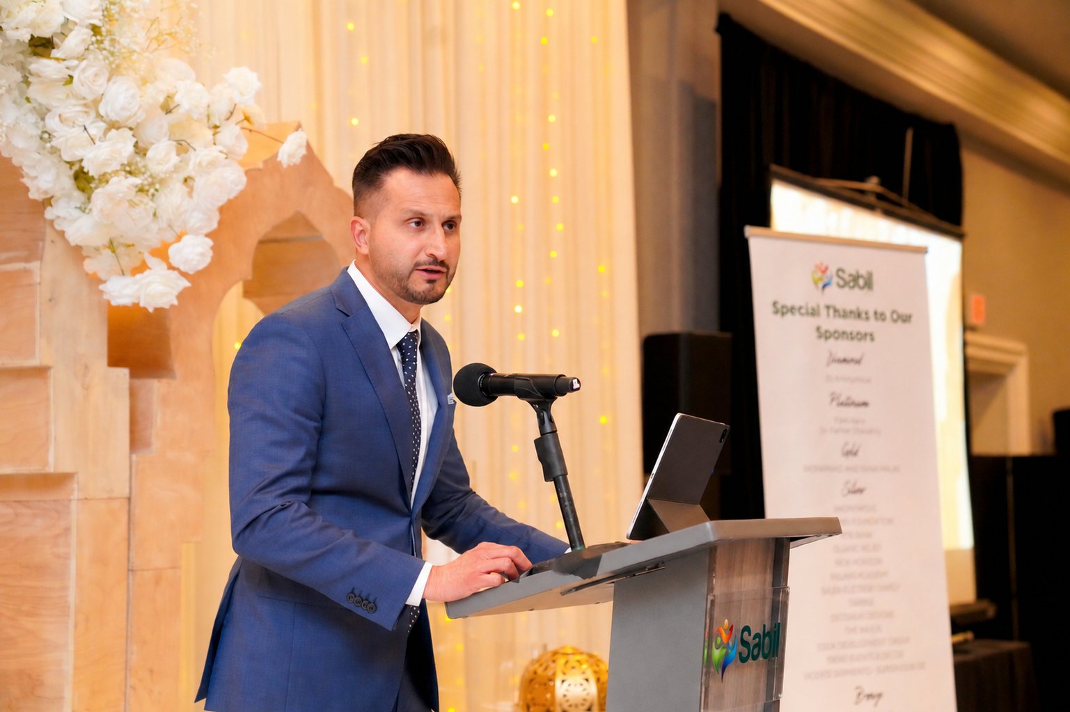 Asim Khan speaking at a lectern during a fundraising banquet