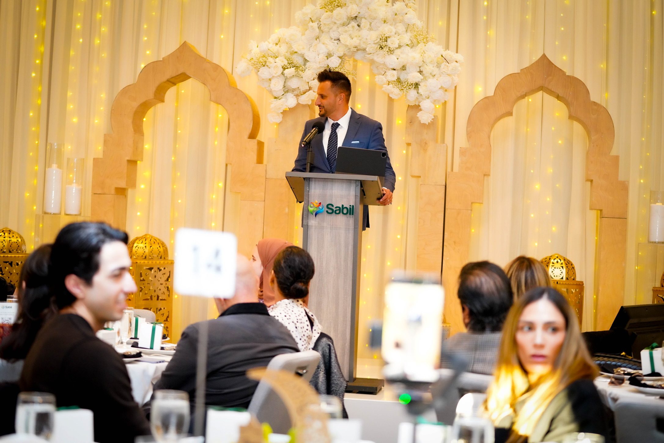 Asim Khan speaking from the lectern to a seated banquet audience