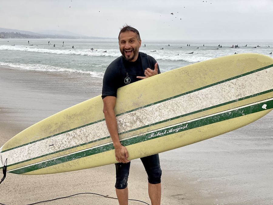 Asim Khan on the beach holding a longboard